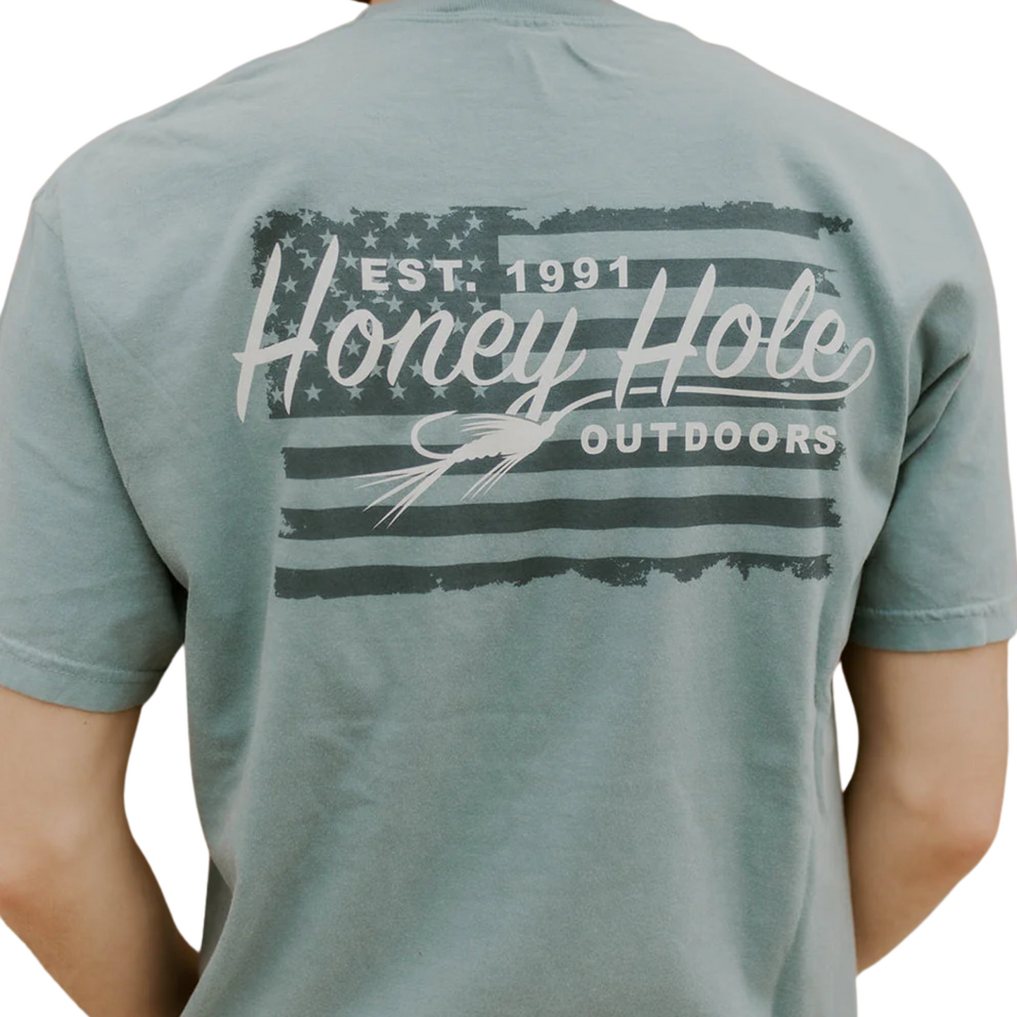 The Honey Hole Outdoors Fly Flag Short Sleeve Tee combines patriotic style with a passion for fishing. Crafted from 100% cotton, it ensures comfort and breathability during outdoor activities. The design features the American flag alongside the Honey Hole Outdoors logo, highlighted by a fishing fly integrated into the script, reflecting your love for angling. Durable and stylish, this tee is ideal for those who value both heritage and their outdoor pursuits.