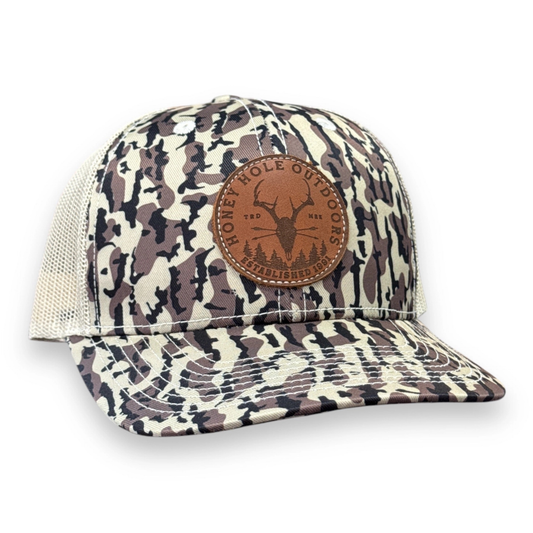 The Leather Dead Shot Snapback Hat combines traditional trucker mesh construction with premium materials. It showcases a leather “Dead Shot” emblem on the front, complemented by Duck Boat Camo fabric and a tan mesh back for enhanced ventilation. Designed for durability and comfort, this hat is perfect for those who demand both style and functionality in outdoor gear.