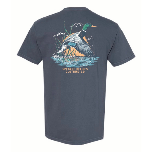 The Mallard Sunrise Short Sleeve Pocket T-shirt by Speckled Bellies features a vivid depiction of a mallard duck taking flight at sunrise, printed on a comfortable 100% cotton, Denim blue fabric. Designed for durability and breathability, this expert-crafted shirt offers both style and practicality, perfect for outdoor enthusiasts and casual wear alike. The added pocket enhances functionality without compromising its sleek look.